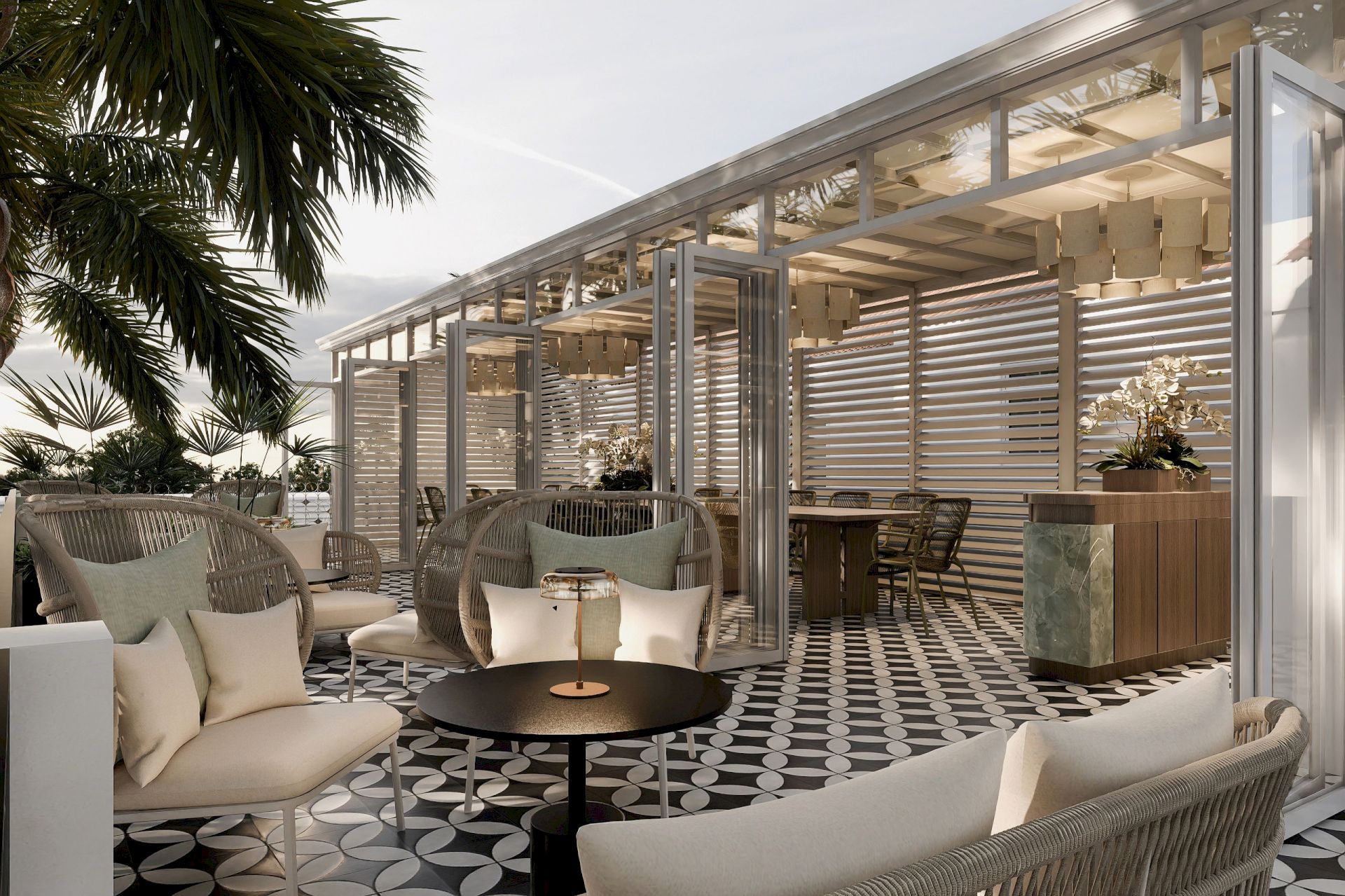 A modern outdoor lounge with beige sofas, a round coffee table, patterned tiles, a glass pergola, and palm trees in view.